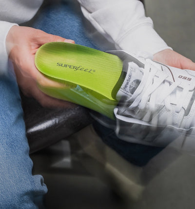 Person holding a white sneaker while inserting a  'Superfeet' insole against a blurred background.
