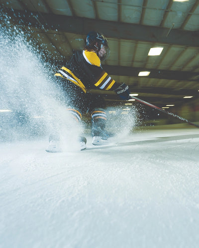Two people playing hockey on an indoor ice rink. 