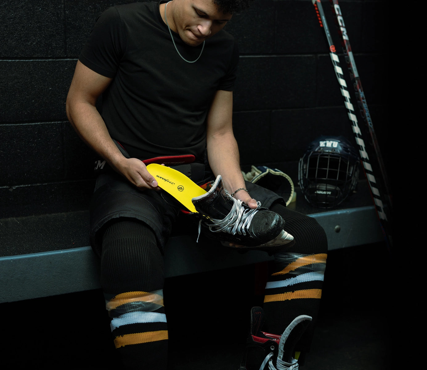 Person sitting on a bench with hockey equipment, while inserting Superfeet's Hockey Performance Insole into a hockey skate. 