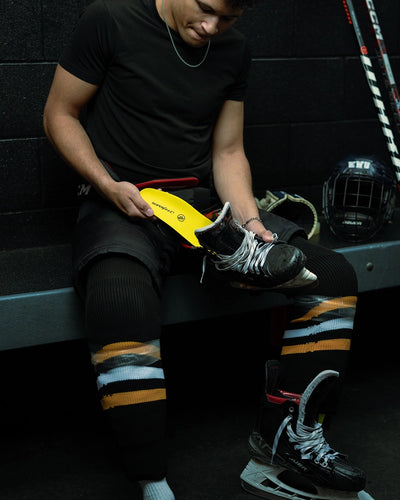 Person sitting on a bench with hockey equipment, while inserting Superfeet's Hockey Performance Insole into a hockey skate. 
