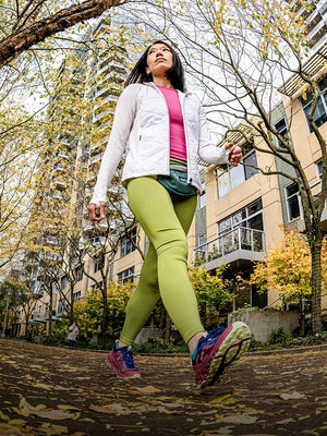 Woman walking outdoors in a city setting with trees and buildings in the background. 