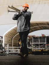 Person in construction attire carrying metal pipes on a construction site. 
